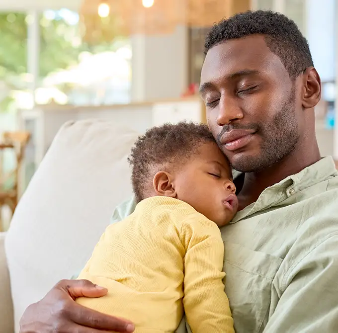 A father cradling his sleeping infant, representing families affected by cystic fibrosis